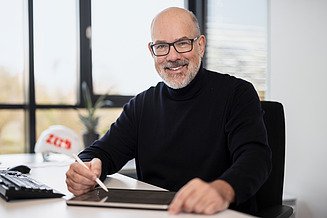 Mitarbeiter mit Tablet sitzt am Schreibtisch