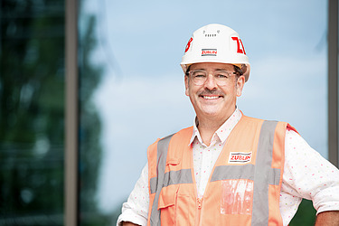 Anställd med bygghjälm och varselväst ler in i kameran.