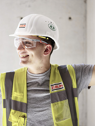 Foto Anställd med varselväst, bygghjälm och skyddsglasögon tittar åt sidan