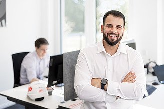 Mitarbeiter steht im Büro und lächelt in die Kamera