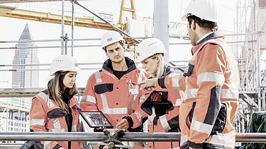 Foto Två medarbetare på en byggarbetsplats, en medarbetare i bakgrunden