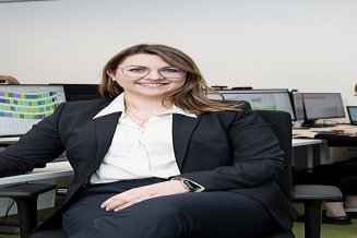 Frau sitzt vor mehreren Bildschirmen und lächelt in die Kamera