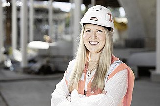 Foto von einer Mitarbeiterin mit verschränkten Armen auf einer Baustelle